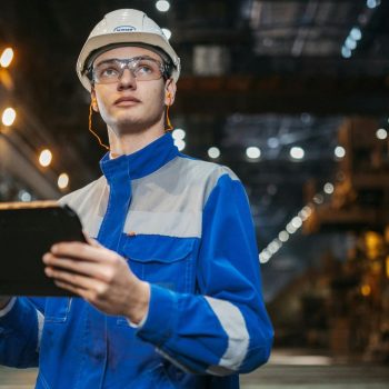 Technicien en usine inspectant les équipements sur tablette dans un environnement industriel pour assurer la maintenance et la continuité de production.