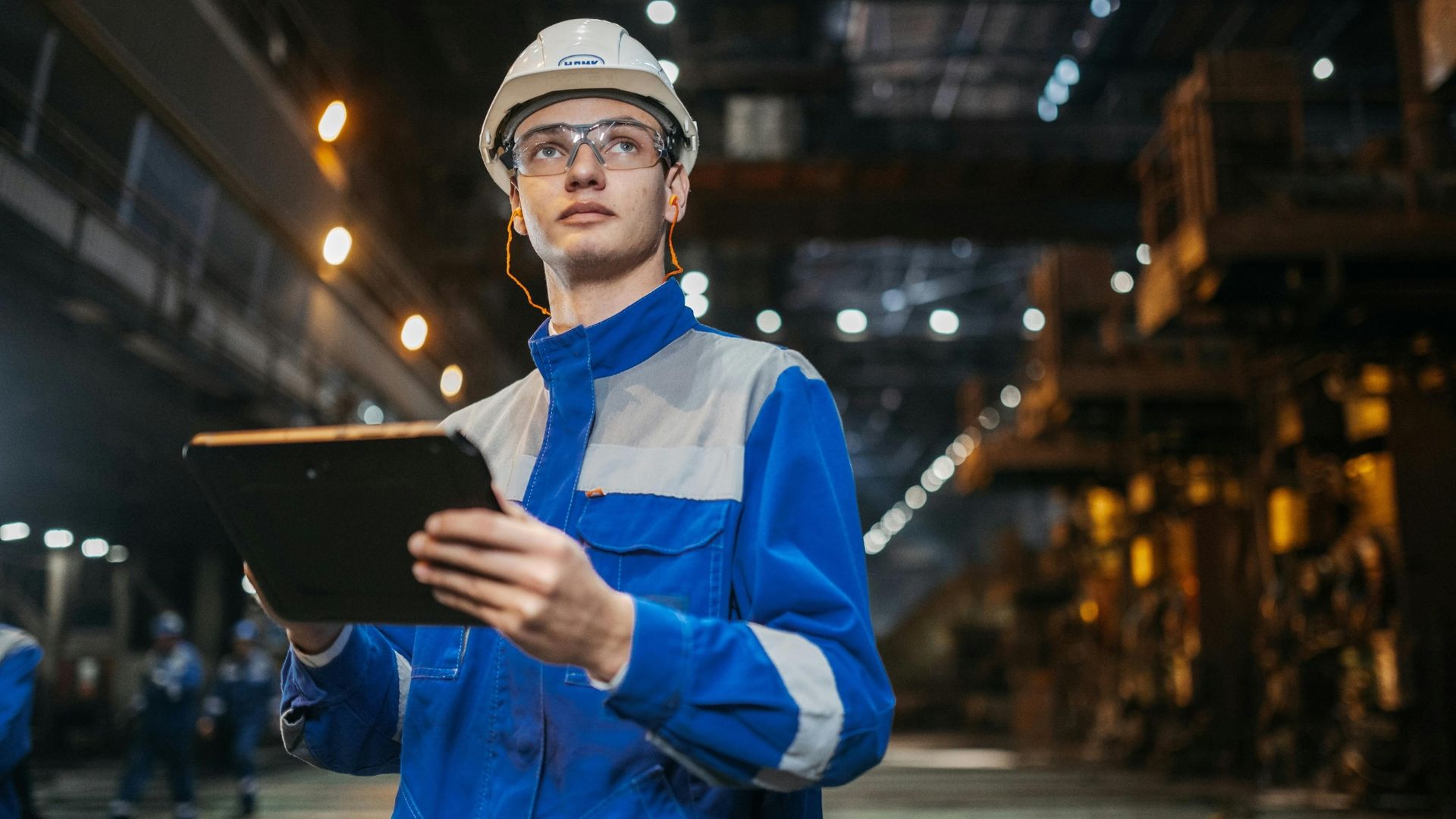 Technicien en usine inspectant les équipements sur tablette dans un environnement industriel pour assurer la maintenance et la continuité de production.